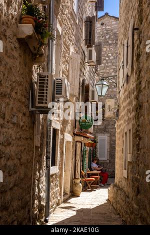Budva, Montenegro - April 29, 2022: A woman sitting at a café table in a narrow street  in Budva old town. Stock Photo