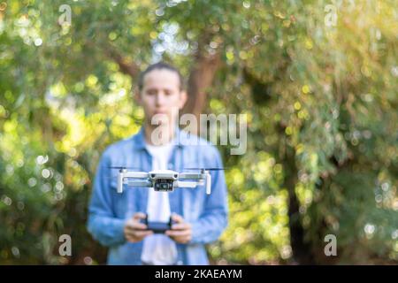 Front view of selective focus on a flying drone with young man controlling it blurred in the background in natural green enviroment Stock Photo