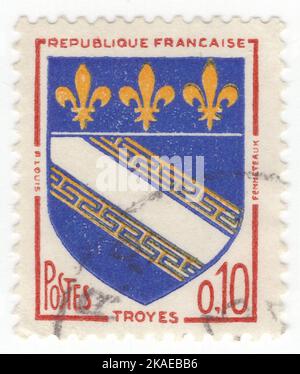 FRANCE - 1963: An 10 centimes red, ultramarine and yellow postage stamp depicting Arms of Troyes, is a commune and the capital of the department of Aube in the Grand Est region of north-central France. It is located on the Seine river about 140 km south-east of Paris. Troyes is situated within the Champagne wine region and is near to the Orient Forest Regional Natural Park. It is the center of the agglomeration community Troyes Champagne Metropole. Troyes developed as early as the Roman era, when it was known as Augustobona Tricassium Stock Photo