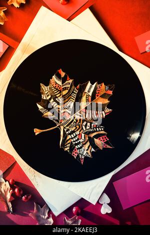 Leaf Art, painted Autumn dry sycamore leaf on vintage vinyl record and paper sleeves on orange, magenta paper background with Autumn decor. Stock Photo