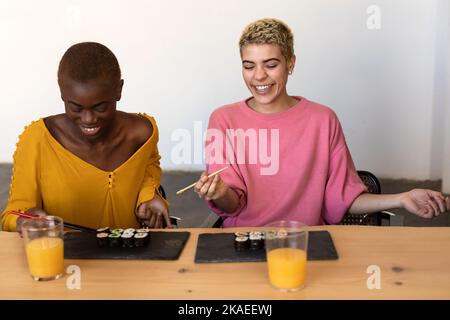 Happy beautiful women sitting while eating vegan sushi rolls Stock Photo