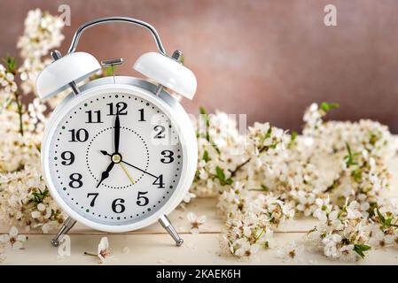 White vintage alarm clock and blossom spring flowers on wooden table. Springtime concept, selective focus. Stock Photo