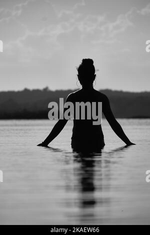 A vertical grayscale shot of the woman's silhouette on the water's surface. Stock Photo