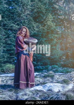 Beautiful shamanic girl playing on african drum drum in the nature. Stock Photo