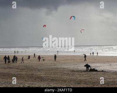 People walking on the beach while windsurfers play in the sea in Saunton Sands in Devon UK Stock Photo