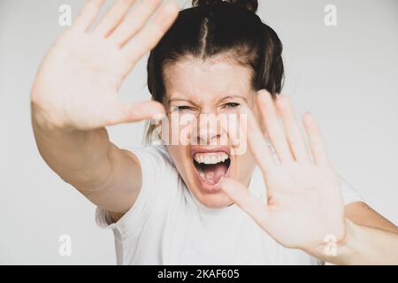 The girl screams and covers her face with her hands isolated background close-up, evil and screaming, stop Stock Photo