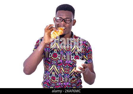 handsome young man having breakfast while eating croissant and holding milk. Stock Photo