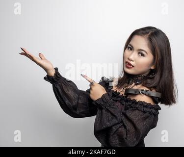 A Filipina in a vampire costume pointing to the side with index finger and palm on white background Stock Photo