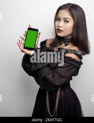 A Filipina in a vampire costume holding a green screen phone on white background Stock Photo