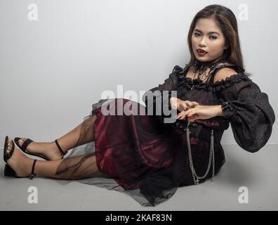 A Filipina in a vampire costume touching her hand while sat on white background Stock Photo