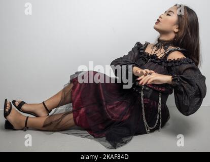 A Filipina in a vampire costume touching her hand and looking up while sitting on white background Stock Photo