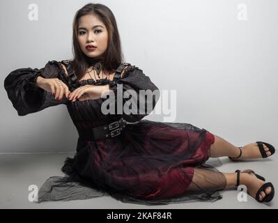 A Filipina in a vampire costume touching her hands while sat on white ground Stock Photo