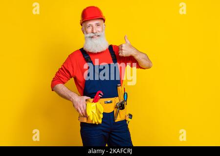 Photo portrait of handsome granddad confident mechanic showing thumb up cheery dressed safety uniform isolated on yellow color background Stock Photo