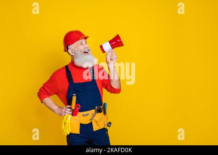 Photo of impressed cool old guy dressed uniform overall red hardhat making announcement empty space isolated yellow color background Stock Photo