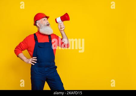 Photo of excited serious age man wear overall uniform red hard hat shouting bullhorn empty space isolated yellow color background Stock Photo