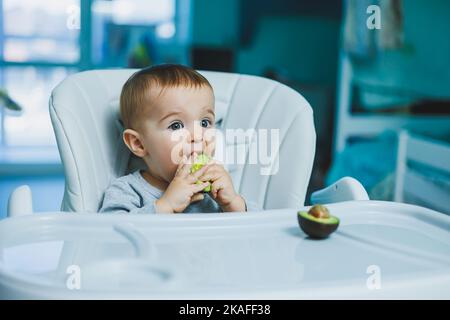 Little adorable baby eating avocado. Vitamin and healthy food for small children. Portrait of beautiful child of 8 months Stock Photo