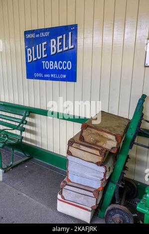 Vintage advertising sign on East Grinstead station building and porter's trolley loaded with suitcases. Bluebell Railway line, East Sussex, England. Stock Photo