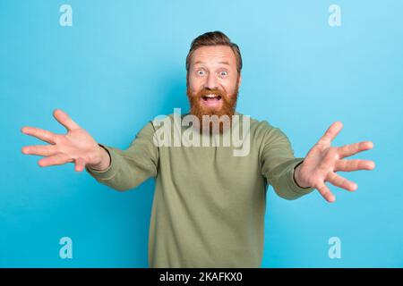 Photo of impressed overjoyed guy with ginger hairdo dressed khaki long sleeve open mouth glad to see you isolated on blue color background Stock Photo