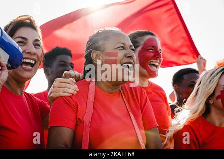 Multiracial red sport football fans celebrating team victory in world championship game at stadium - Soccer supporters having fun in crowd - Focus on Stock Photo