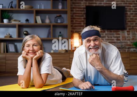 Gray-haired happy mature elderly couple doing gymnastics together at home. Active and healthy lifestyle for pensioners. Fitness, recreation, well Stock Photo