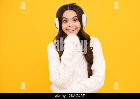 Modern teenage girl 12, 13, 14 year old wearing sweater and winter warm earmuff ear-flaps hat on isolated yellow background. Stock Photo