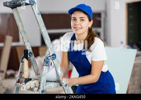 Positive young female builder contractor inspecting room and taking notes Stock Photo