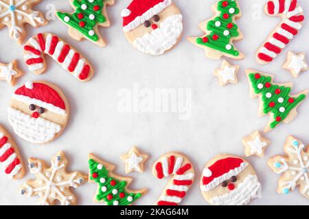 Cute Christmas cookie frame. Top down view on a white marble background with copy space. Holiday baking concept. Santa Claus, tree, snowflakes, candy Stock Photo