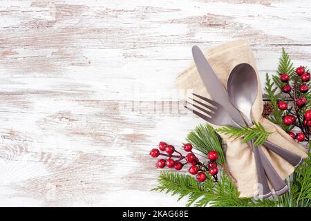 Christmas or winter table setting corner border. Cutlery and napkin  with evergreen branches and red berries. Top down view on a white wood background Stock Photo