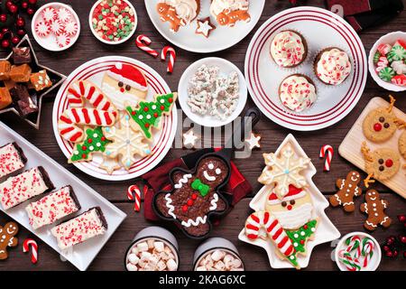 Cute Christmas sweets and cookie table scene. Overhead view on a rustic dark wood background. Fun holiday baking concept. Stock Photo