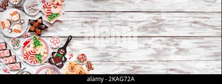 Cute Christmas sweets and cookie corner border. Above view over a rustic white wood banner background with copy space. Fun holiday baking concept. Stock Photo