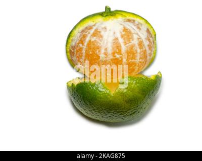 Unripe tangerine. Peeling a tangerine. Green fruit on a white background. Sour ingredient. Citrus isolate. Useful fruit. Stock Photo