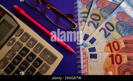 Euro money, Euro with calculator, pen or pencil and glasses on the purple notebook backgorund, top view photo. Stock Photo