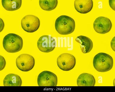 Unripe tangerine on a yellow background. Peeling a tangerine. Green and yellow color. Sour ingredient. Citrus isolate. Sliced tangerine. Useful fruit. Stock Photo