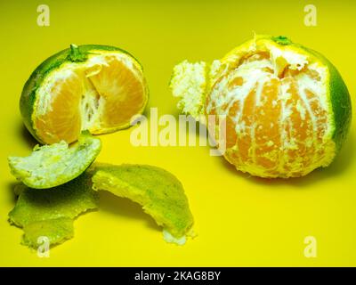 Unripe tangerine on a yellow background. Peeling a tangerine. Green and yellow color. Sour ingredient. Citrus isolate. Sliced tangerine. Useful fruit. Stock Photo