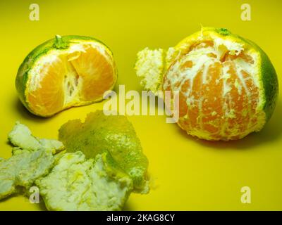 Unripe tangerine on a yellow background. Peeling a tangerine. Green and yellow color. Sour ingredient. Citrus isolate. Sliced tangerine. Useful fruit. Stock Photo