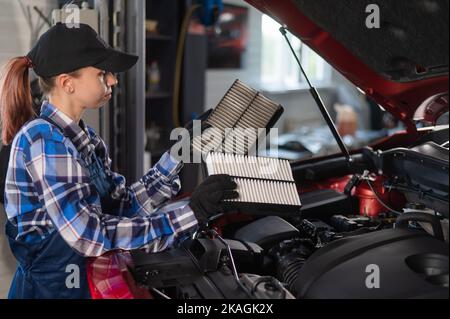 Caucasian female auto mechanic changes the engine air filter in the car. Stock Photo