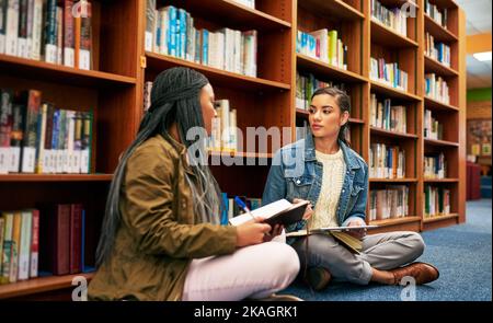 Getting together on their group project. two university students working together in the library at campus. Stock Photo
