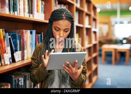 Education through the digital sphere. a university student using a digital tablet in the library at campus. Stock Photo
