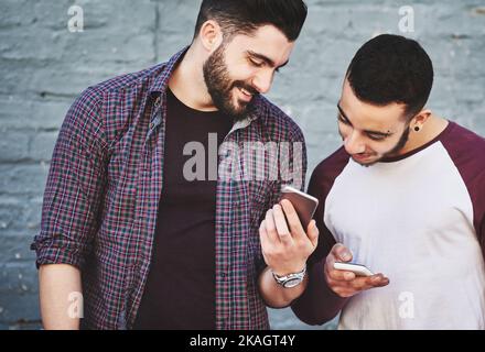 Remember this. two young men standing outdoors and using a mobile phone against a gray wall. Stock Photo