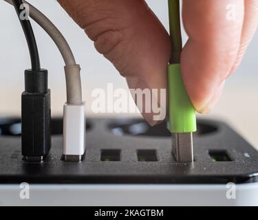 Modern convenient multi-port usb charger for devices. Close-up of a female hand plugging multi-colored cables into a power outlet. Macro. Stock Photo