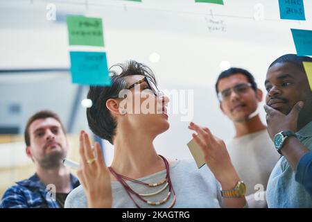 We will succeed if we write down our plans. a group of designers brainstorming with notes on a glass wall in an office. Stock Photo