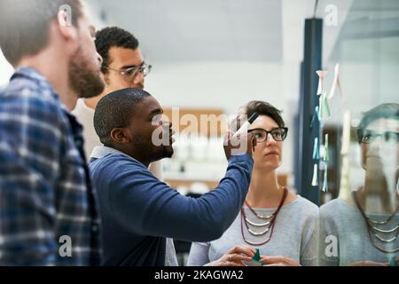 Putting big plans into place then action. a group of designers brainstorming with notes on a glass wall in an office. Stock Photo
