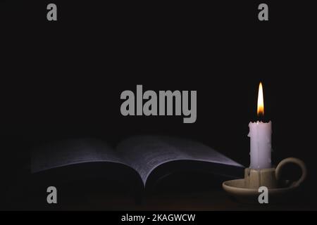 The brightly burning candle on the candlestick, the holy bible, and the words of worship, meditation and prayer of Jesus Christ Stock Photo