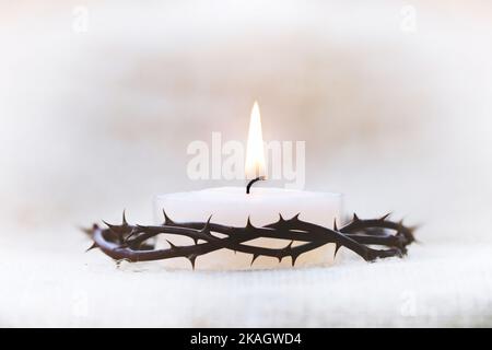 Crown of thorns symbolizing the suffering cross, death and resurrection of Jesus Christ and brightly shining candle background Stock Photo