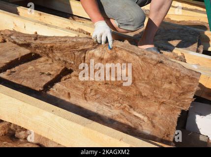 Roofer contractor checking mineral wool insulation on house roof for energy saving. Roofing construction with thermal glass wool insulation. Stock Photo