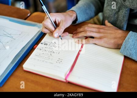 Working on some mathematical equations. High angle shot of an unrecognizable university student writing in his notebook while sitting in class. Stock Photo