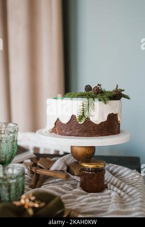 Festive Christmas cake with white icing decorated with spruce branches stands on a set table Stock Photo