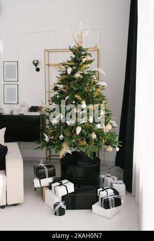 Stylish Christmas tree with black and white toys, which stands on an iron barrel in the living room of the house Stock Photo