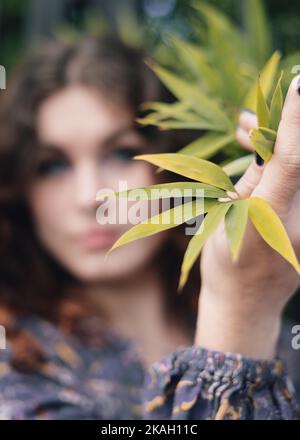A woman holds a bamboo leaf in one had. Focus is on the bamboo leaf. Stock Photo