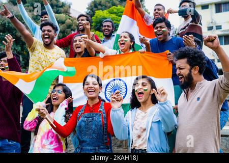 Group of audience at stadium shouting, screaming for win by holding indian flags while watching crcket sports match at stadium - concept of Stock Photo